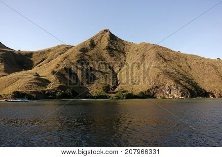 Small boat in front of coastline of mountains with green vegetation reflected in blue ocean water at Labuan Bajo in Flores Indonesia.