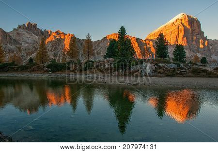 Mountain rocks and autumn trees reflected in water of Limides Lake near Cortina d'Ampezzo at sunset Dolomite Alps Italy