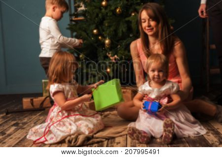 Blurred image of Happy cheerful mother and children sitting next to Christmas tree with gifts. Loving parent and kids having fun together at home. Merry Christmas and Happy holidays.