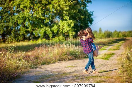 a young happy couple strolls along the field road poren holds a cup in her hands and kisses
