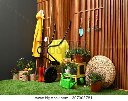 Gardening Tools With Wheelbarrow And Flowers Near Wooden Wall