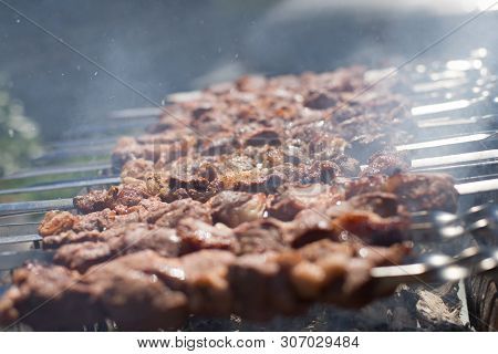Shashlik Or Shashlyk Preparing On A Barbecue Grill Over Charcoal. Grilled Cubes Of Pork Meat On Meta