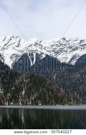 Lake Ritsa In Abkhazia In Spring. The Mountain Tops Are Covered With Snow. The Beginning Of The Tour