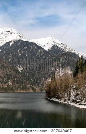 Lake Ritsa In Abkhazia In Spring. The Mountain Tops Are Covered With Snow. The Beginning Of The Tour
