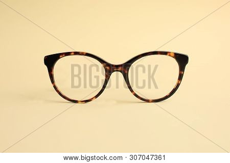 Modern Fashionable Acetate Spectacles, Torture Color Laying On Light Yellow Background.