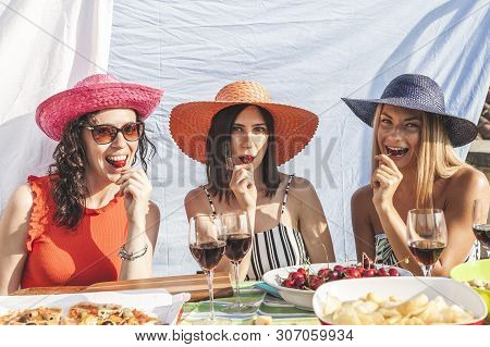 Group Of Female Friends Having Fun While Eating Cherries On The Roofs Among Hanging Laundry - Concep