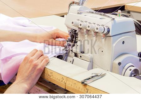 Industrial Overlock Sewing Machine And Hands Of Seamstress At Work In The Garment Factory