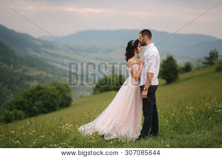 Beautiful Young Wedding Couple Standing On The Green Slope, Hill. Groom And Bride In Carpathian Moun