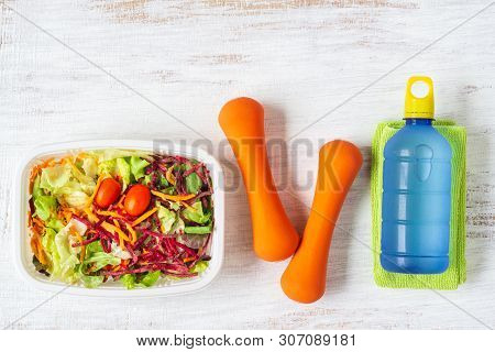 Fresh Vegetable Salad In Lunch Box With Orange Dumbbells Excercise Equipment And Energy Water Drink 