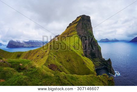 Small White Kallur Lighthouse Located Near Huge Cliffs On Island Of Kalsoy. Kalsoy Is An Isolated Sm