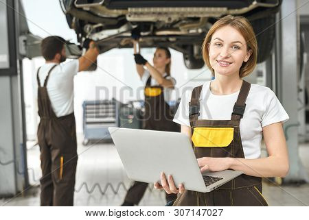 Front View Of Attractive Woman Working At Auto Service. Professional Engineer In Coverall Keeping Co