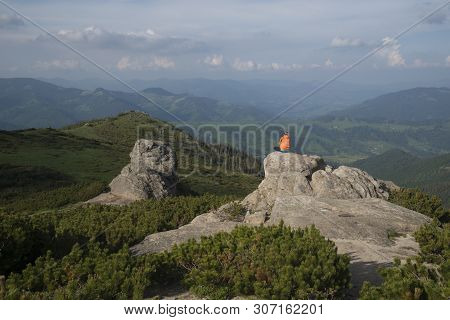 Girl In Orange Jacket Sits On A Rock And Meditates, Contemplating The Landscape.