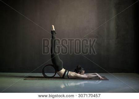 Woman Practicing Yoga, Doing Salabhasana Pose With Wheel.