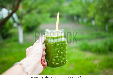 woman's hand holding a jar with green cold-pressed juice, nature background. Healthy eating, detoxing, juicing, body cleancing concept 