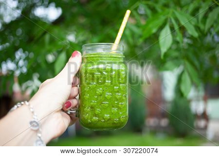 woman's hand holding a jar with green cold-pressed juice, nature background. Healthy eating, detoxing, juicing, body cleancing concept 