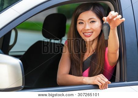 Beautiful Chinese Asian young woman or girl leaning out of a car in summer sunshine smiling with perfect teeth and long hair holding a car key. Car hire, driving test or vacation concept.
