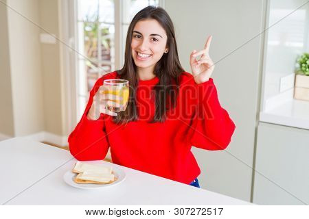Beautiful young woman eating toasts and orange juice for snack or breakfast very happy pointing with hand and finger to the side