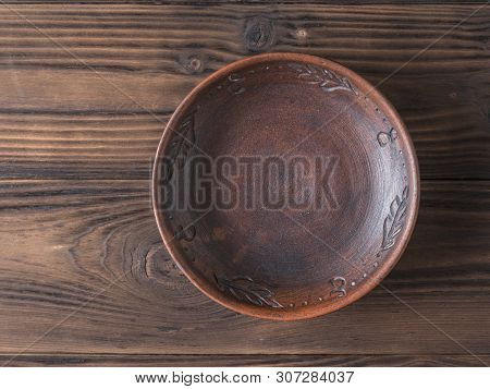 Clay Bowl On A Brown Wooden Table. The View From The Top. Pottery For The Kitchen. Flat Lay.