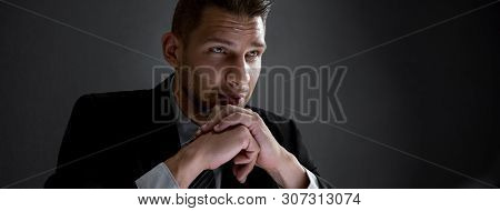 Thoughtful Serious Businessman With Hands On Chin In Dark Banner Background With Copy Spacce