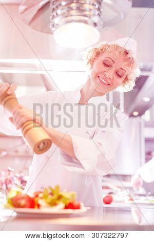 Smiling mature chef using peppermill on salad in plate at restaurant