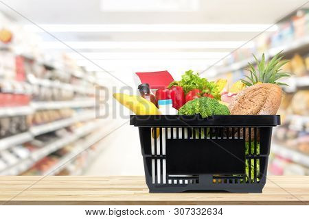 Food And Groceries In Shopping Basket On Wood Table With Blurred Suppermarket Aisle In Background