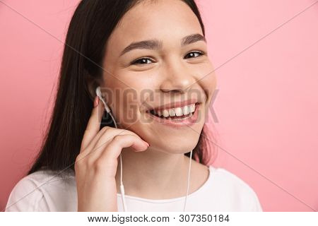 Portrait closeup of optimistic european girl wearing earphones smiling while listening to music isolated over pink background