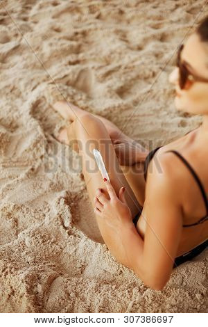 Sunscreen Suntan Lotion In Spray Bottle. Young Woman In Spraying Tanning Oil On Her Leg From Bottle.