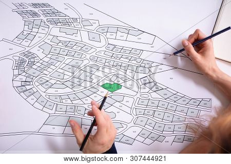 Close-up Of Human Hand Holding Pencil Over Paper Cadastre Map