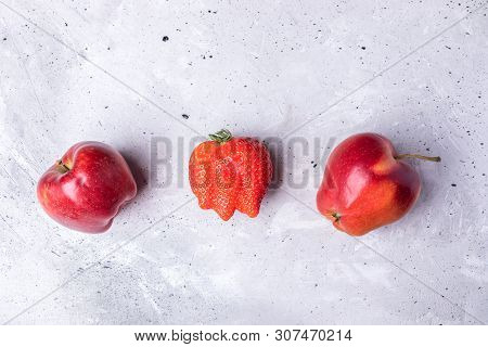 Three Ugly Fruits: Strawberry And Two Apples On Concrete Background.