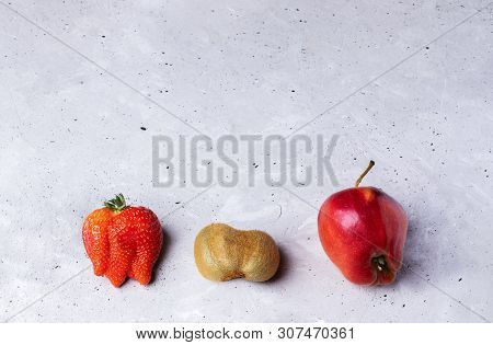 Three Ugly Fruits: Strawberry, Kiwi And Apple On Grey Concrete Background.