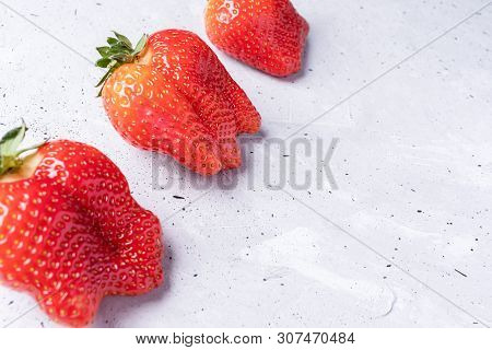 Three Ugly Red Strawberries Are Lying Diagonally On Concrete Background.