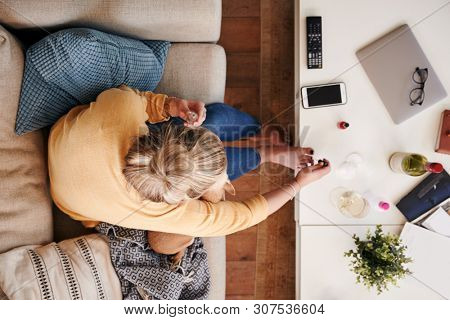 Overhead Shot Looking Down On Woman At Home Lying On Sofa Painting Toe Nails