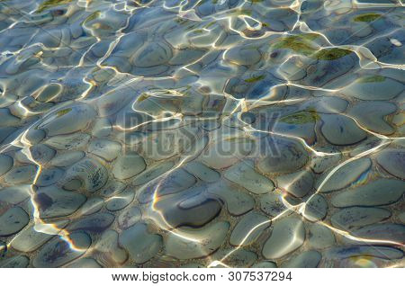 Close Up Of Sunny Water Ripples Over Grey Rocks.  Clear Water With Sunlit Ripple Patterns. Rocks Und
