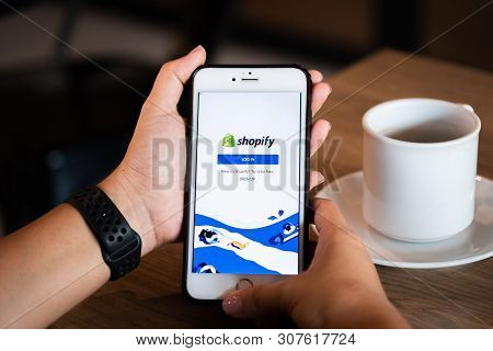 Chiang Mai / Thailand - June 22 2019 : Hands Holding Mobile With Shopify Screen In Coffee Shop.