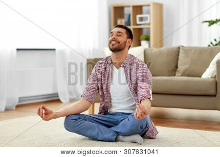 mindfulness, meditation and relaxation concept - man meditating in lotus pose at home