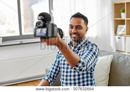 blogging, videoblog and people concept - smiling indian male video blogger with camera videoblogging at home