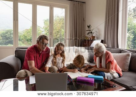 Front view of Caucasian grandparents helping grandchildren with homework in living room at comfortable home