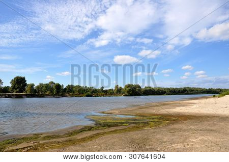 Wide Blue River Is Slow Flowing. Summer. Sunny Weather And White Sand. Green Trees Far Away