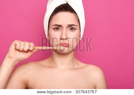 Horizontal Shot Of Upset Woman Holding Toothbrush And Brushing Her Teeth Isolated Over Pink Backgrou