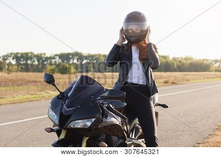Outdoor Shot Of Attractive Confident Moto Driver With Helmet Wearing For Safety, Sitting On Her Moto