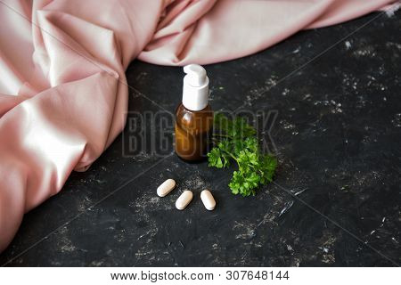 Glass Bottle With Essential Oil Or Creme, Vitaminen And Healing Green Herbs On The Rough Texture Bac
