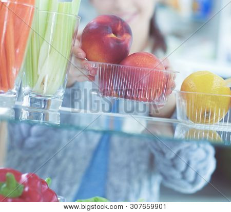 Portrait Of Female Standing Near Open Fridge Full Of Healthy Food, Vegetables And Fruits. Portrait O