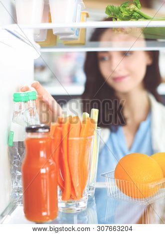 Portrait Of Female Standing Near Open Fridge Full Of Healthy Food, Vegetables And Fruits. Portrait O