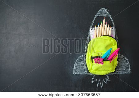 Back To School Concept With Small Bag Backpack, School Supplies And Rocket Sketch Over Chalkboad Bac