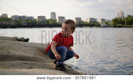 Boy Quatting By The Still Pond In Red T-shirt And Looking Back