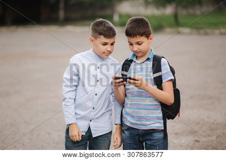 Two Boys Plays Online Games After School Classes. Young Boys Smile And Use Phone