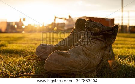 Safety Boots At A Construction Site Covered In Mud In Front Of A Bright Sunset
