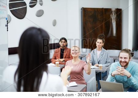 Wide Angle Portrait Of Smiling Mature Woman Raising Hand In Class With Group Of Student Enjoying Lec