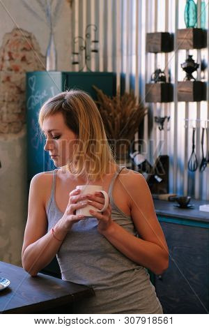 A Beautiful Freckled Blonde Girl In Pajamas Is Standing Near The Kitchen Table, Drinking Fock, Tea A