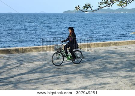 Wonsan, North Korea - May 3, 2019: Local Woman On A Bike Rides Along The Sea On The Promenade Of The
